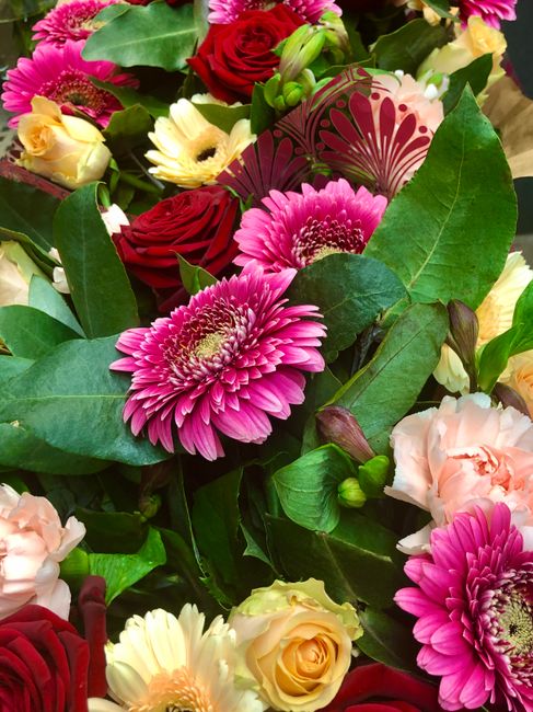 A vibrant floral arrangement featuring bright pink gerbera daisies with layered petals and prominent yellow centers, surrounded by deep red roses with velvety petals, soft peach-colored lisianthus wit